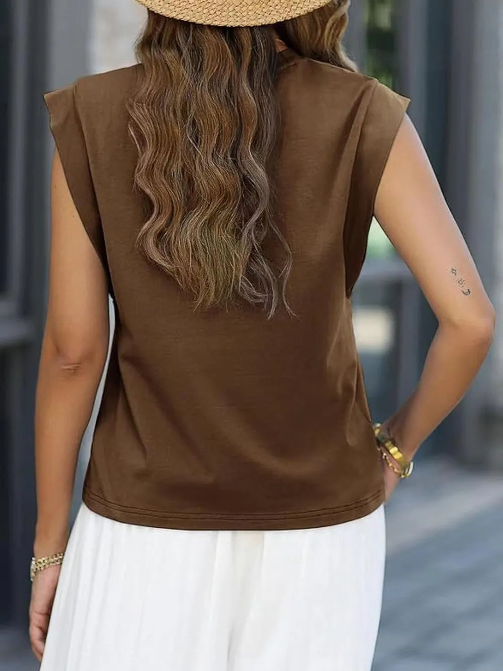 Person wearing a brown sleeveless top and white pants with a blurred background