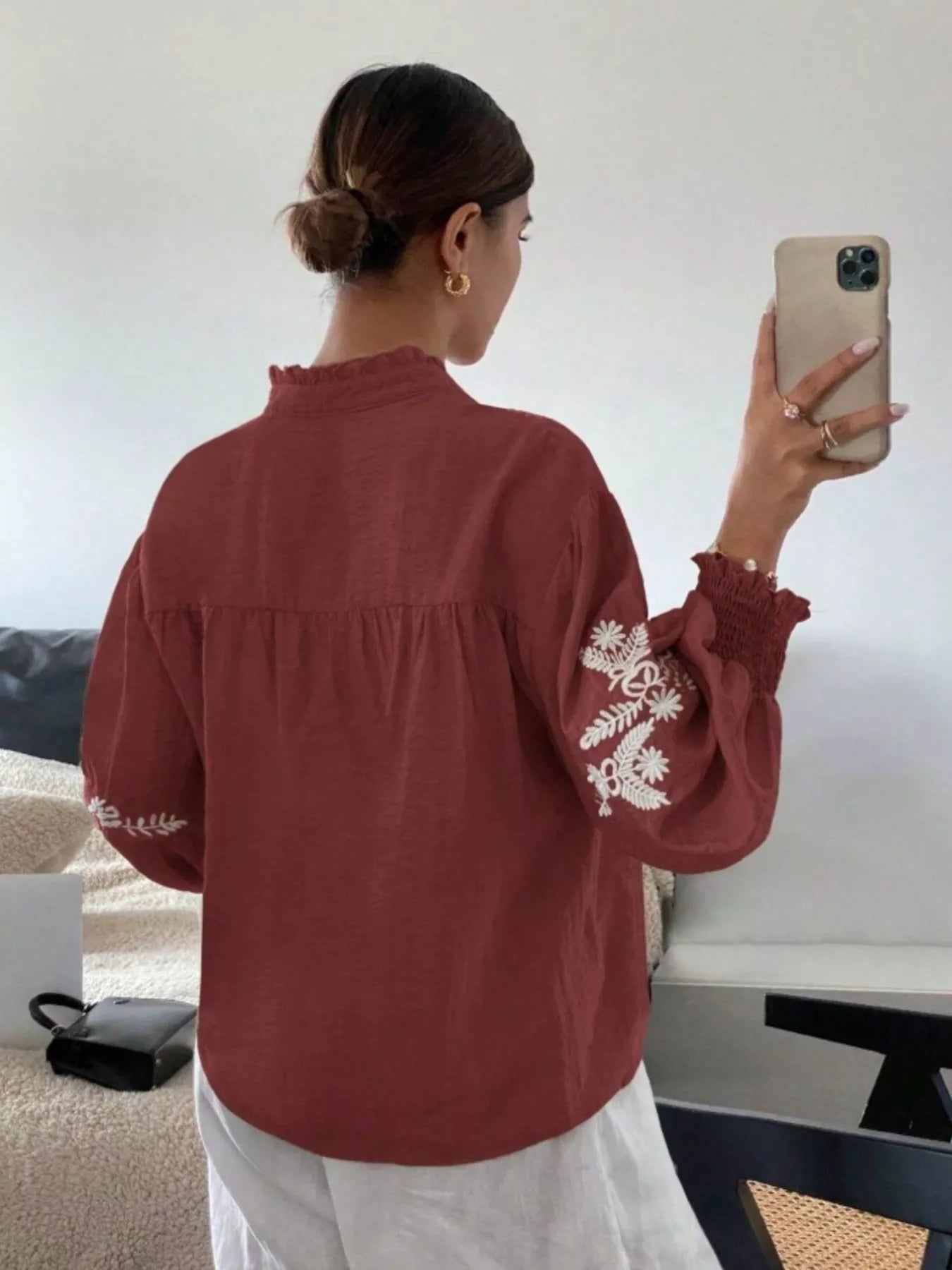 Person wearing a red blouse with white embroidery, taking a mirror selfie.
