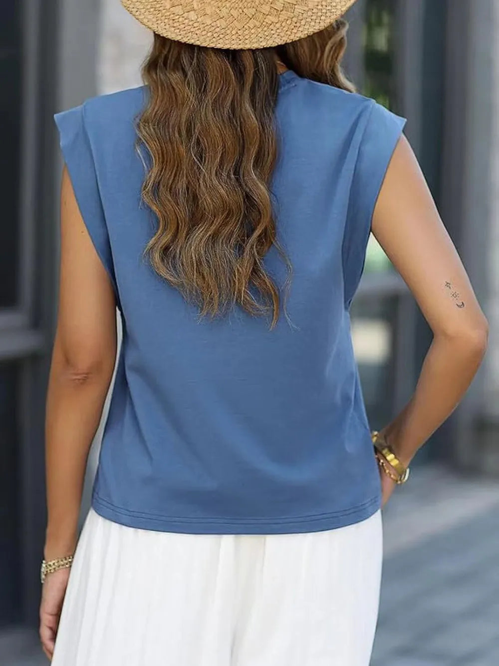 Person wearing a blue sleeveless top and white pants with a straw hat, standing outdoors.