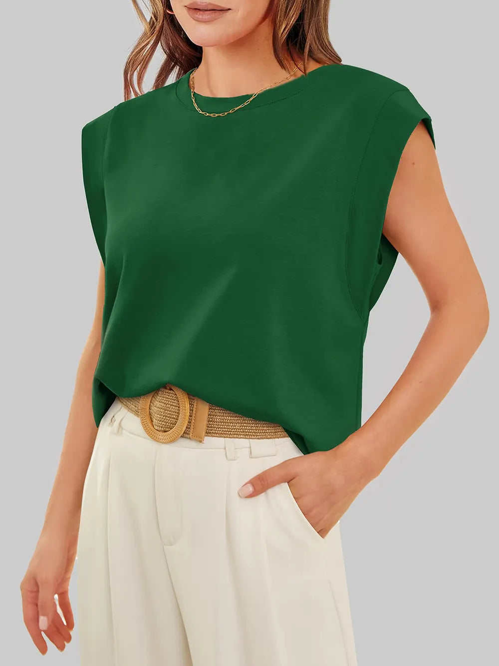 Woman wearing a green sleeveless top and beige pants against a gray background