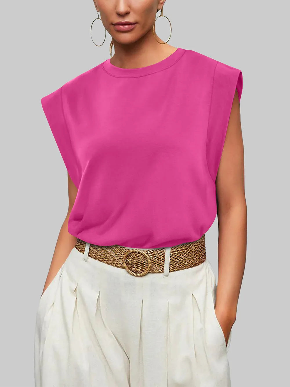 Person wearing a bright pink sleeveless top and white pants with a belt, on a plain background