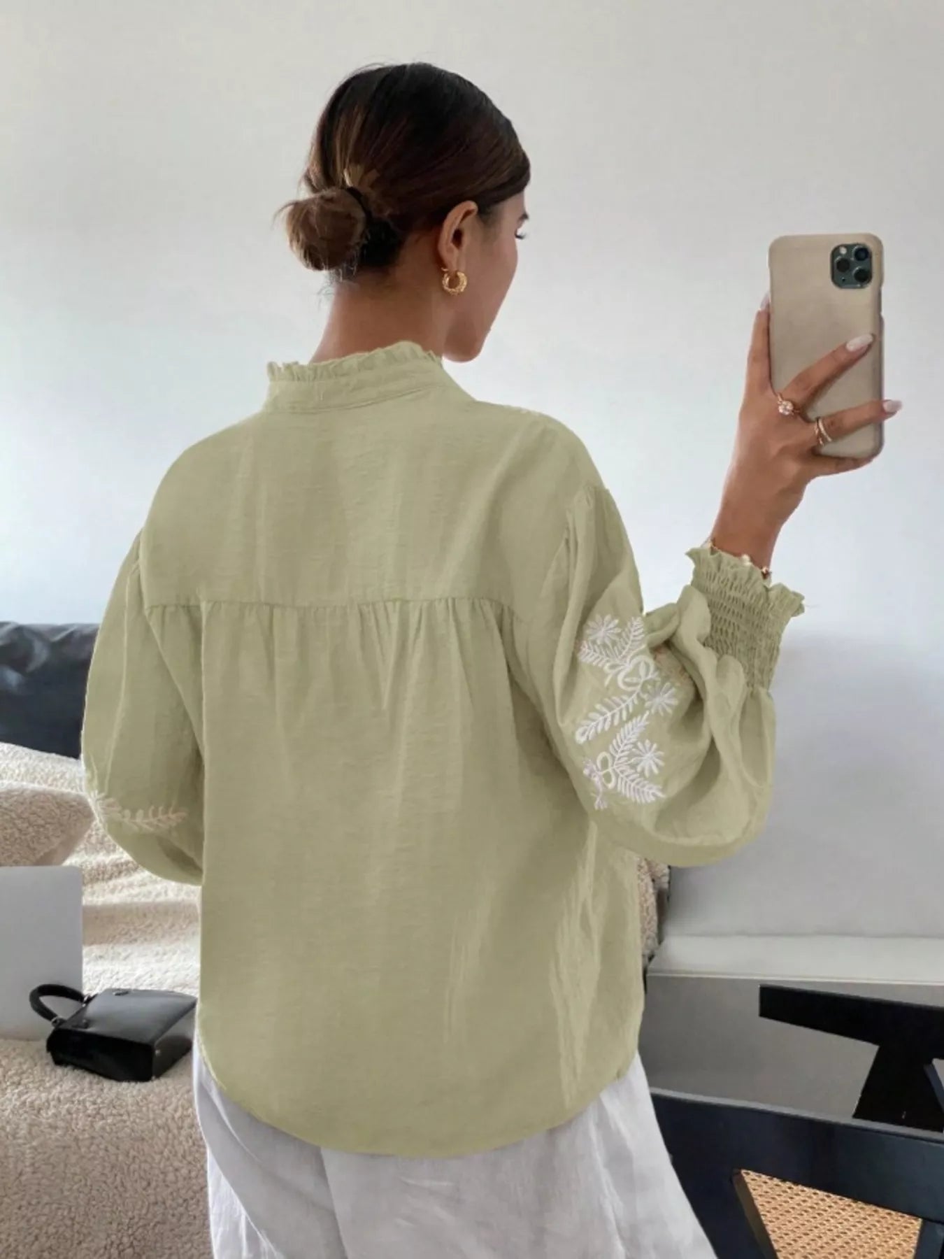 Woman taking a selfie wearing a light green blouse with lace sleeves in a room.