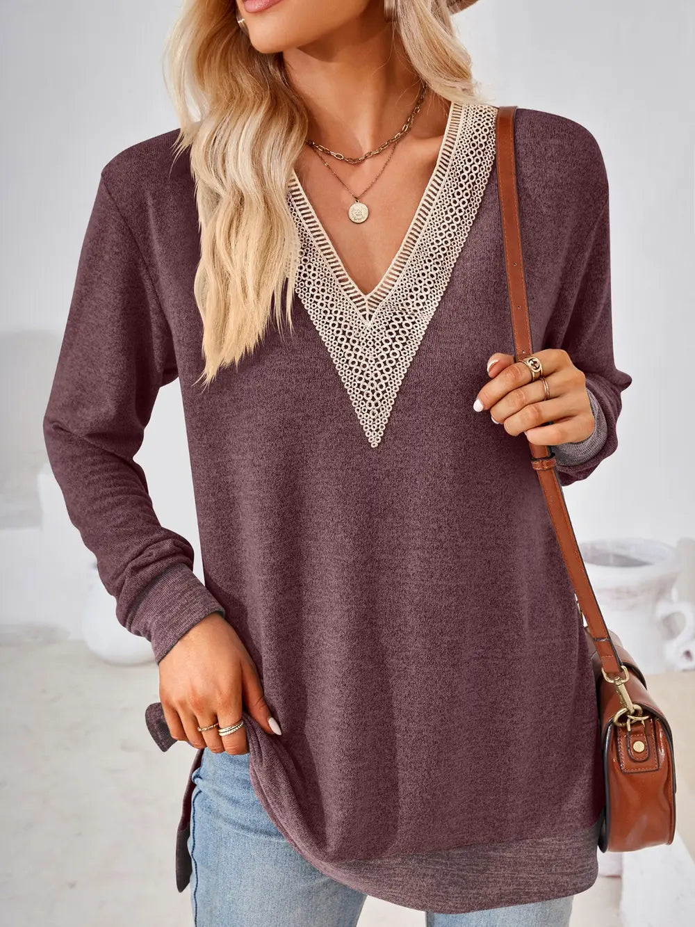 Woman wearing a maroon sweater with lace neckline holding a brown handbag.