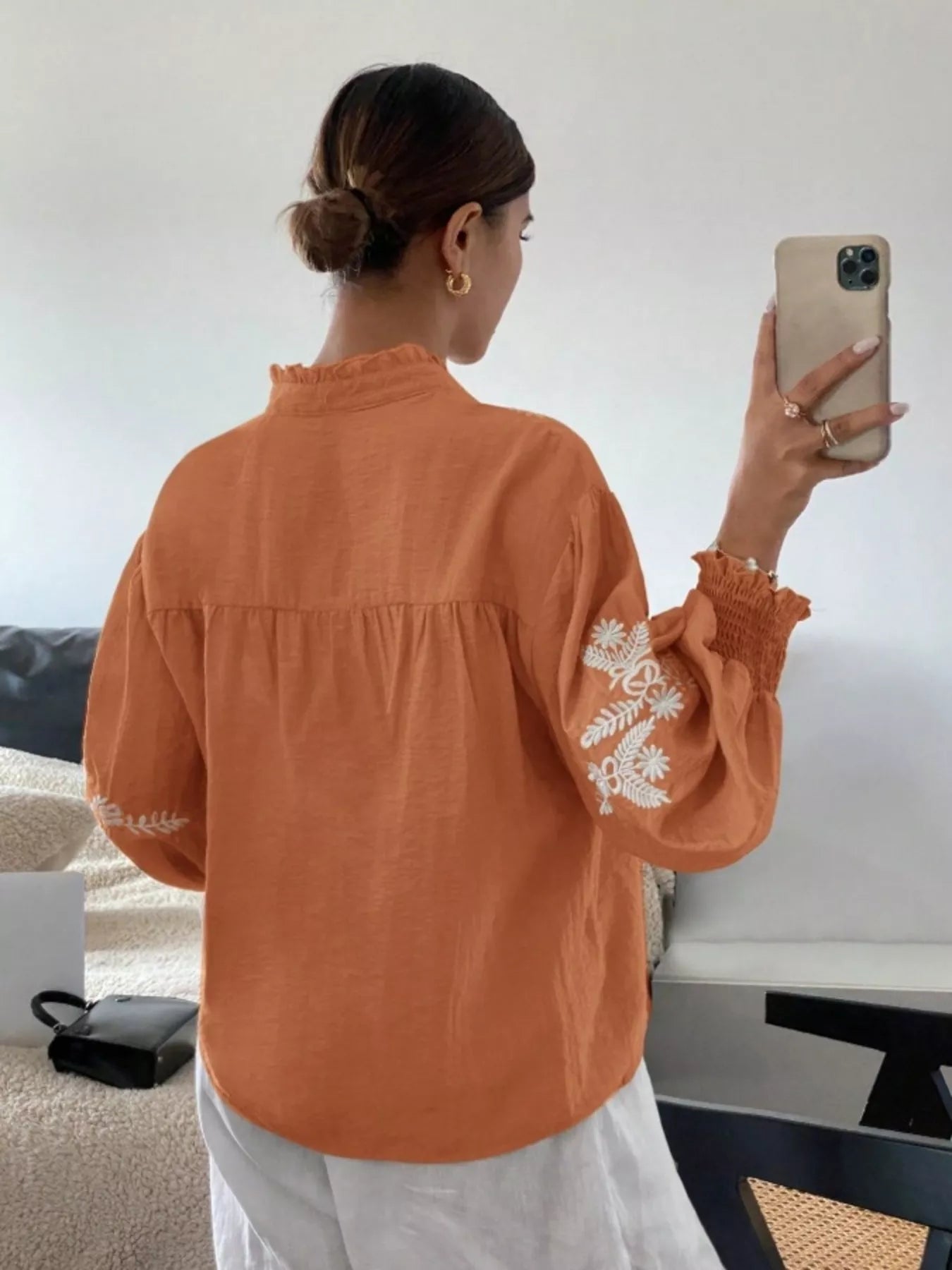 Person wearing an orange blouse with white lace sleeves, taking a selfie.