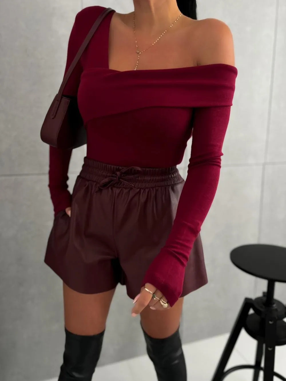Person wearing a burgundy off-shoulder top and shorts with black knee-high boots against a neutral background.
