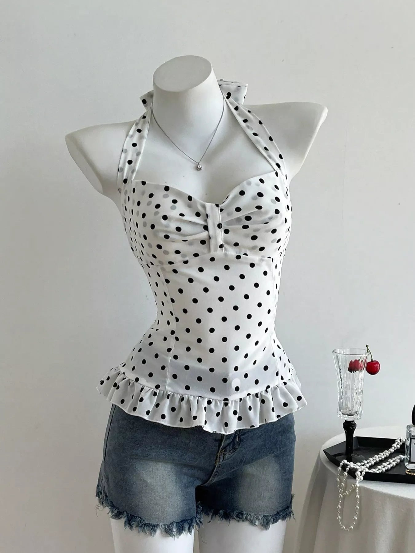White top with black polka dots on a mannequin with denim shorts, against a plain background.