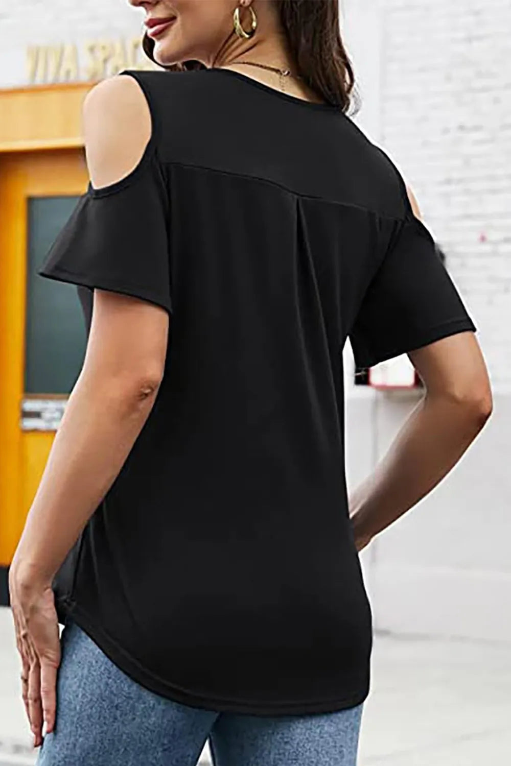 Woman wearing a black cold-shoulder top with a blurred indoor background