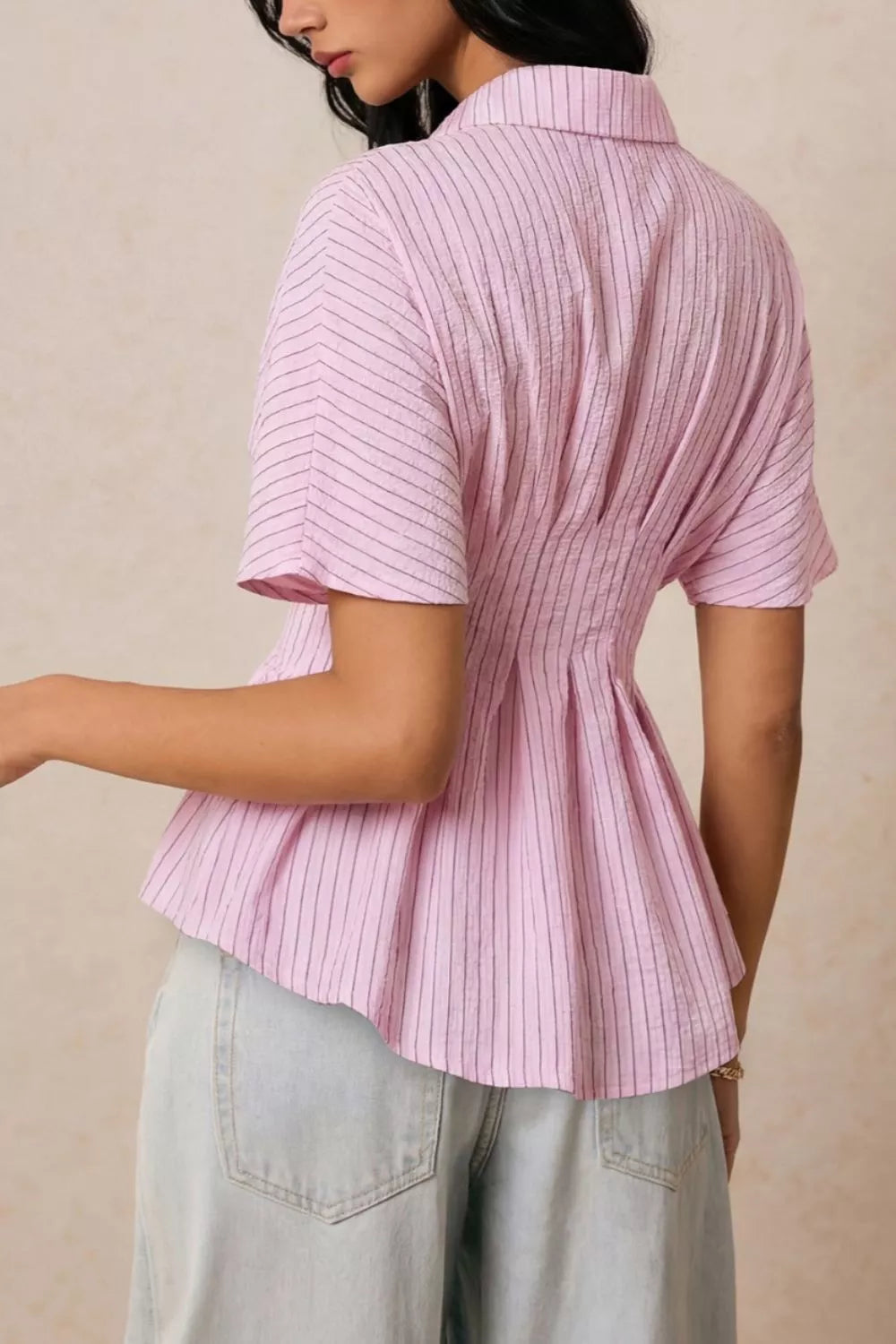 Side view of blush pink striped peplum button up shirt showcasing tailored waistline and flared hem
