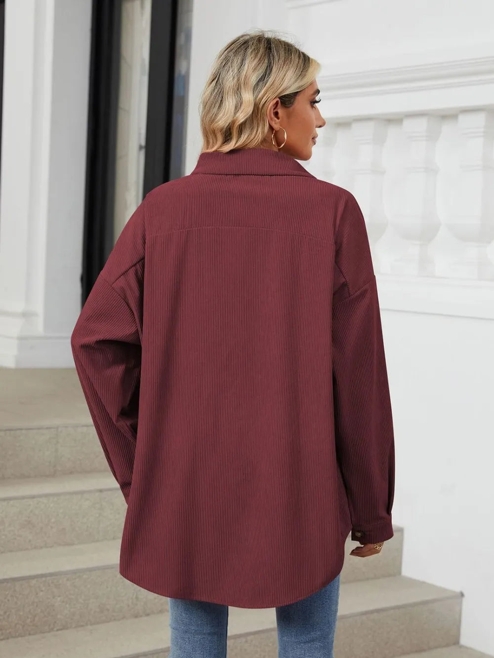 Person wearing a burgundy coat standing in a room with white walls and a staircase.