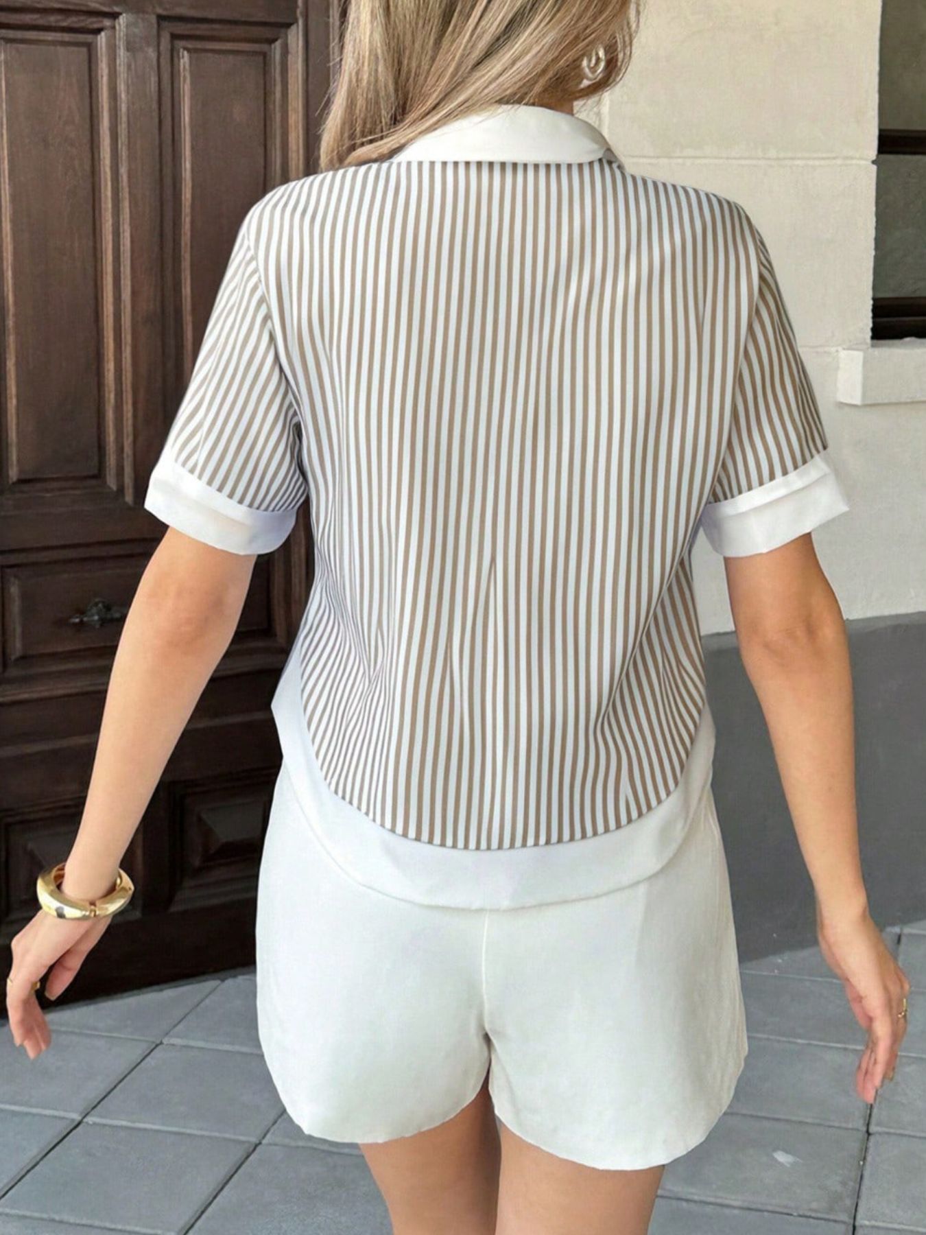 Person wearing a striped shirt and white shorts walking on a tiled floor.
