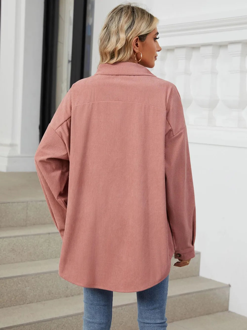 Person wearing a pink coat standing on steps with a white wall in the background
