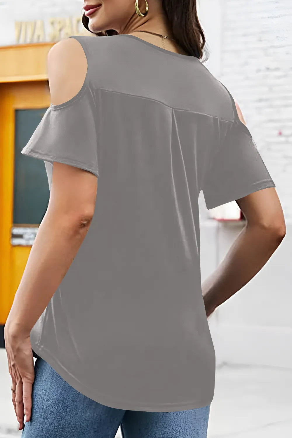 Woman wearing a gray off-shoulder top with a blurred indoor background