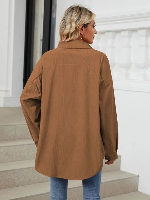 Person wearing a brown coat standing on steps with a white wall in the background