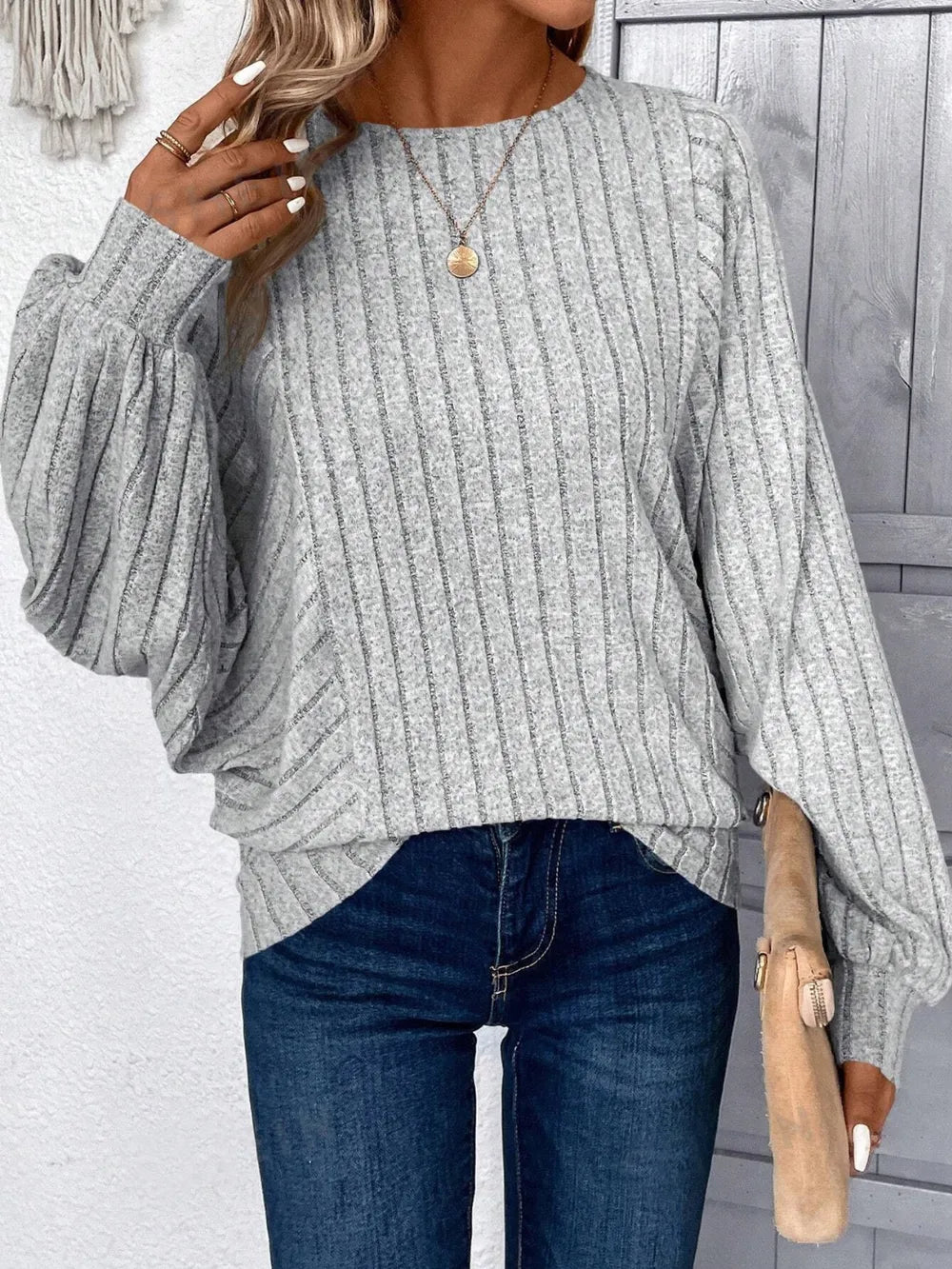 Person wearing a gray ribbed sweater and blue jeans with a blurred background