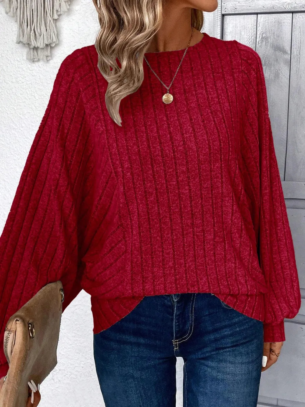 Person wearing a red sweater and blue jeans with a neutral background