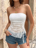Woman wearing a white lace top and denim shorts with a stone wall background