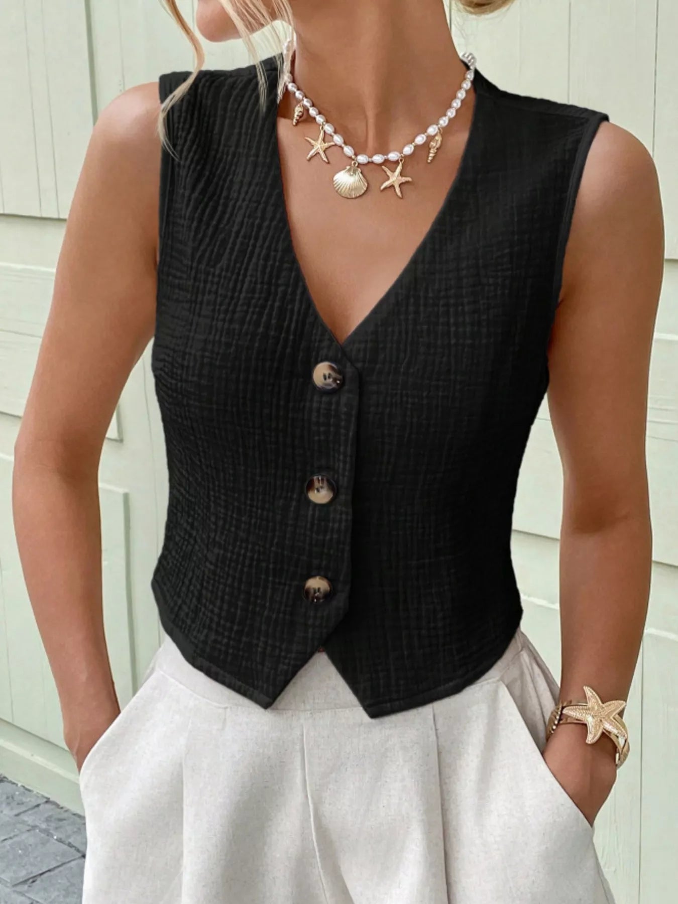 Close-up of the V-neckline and button-front detail on a black textured cotton vest top